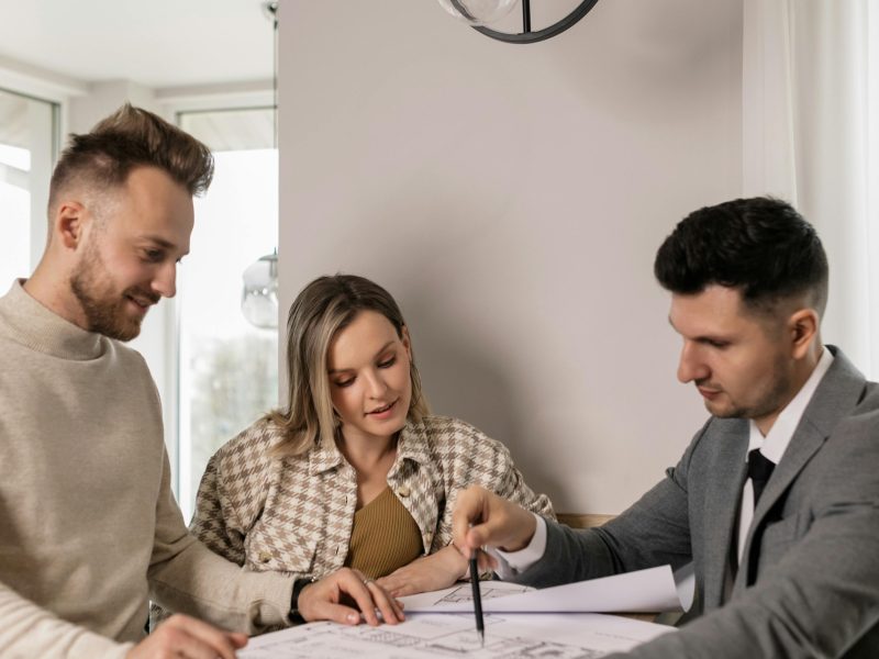 Couple discussing a blueprint with a real estate agent, planning their new home purchase.