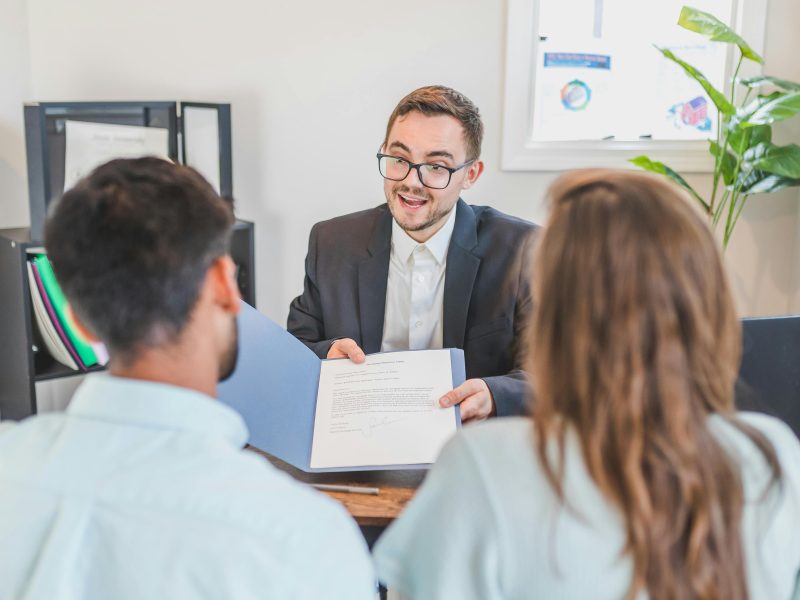 A businessman discusses a contract with clients in a modern office setting.