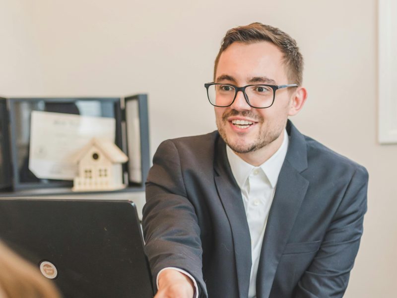 A professional real estate agent welcomes a client in the office with documents on the desk.