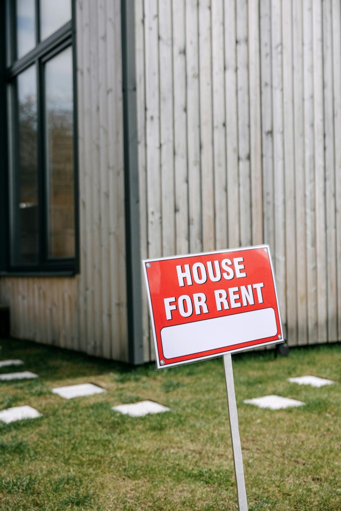 Red 'House for Rent' sign in front of a modern wooden house exterior.